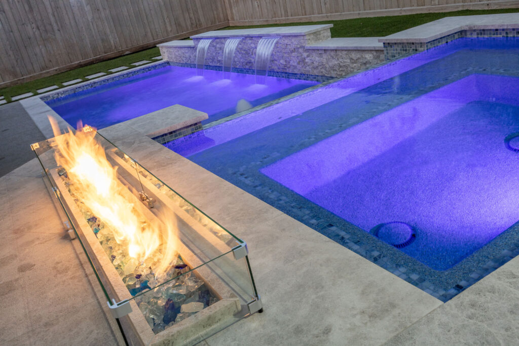 Custom pool with glass fire feature and spa lit at night